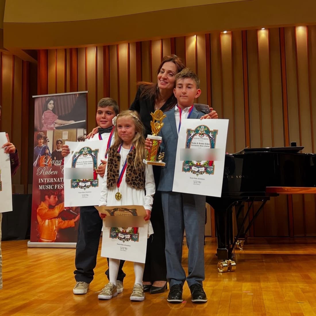 Three ABA Music Academy students on stage with their certificates and trophy at the Liana & Ruben Cohen International Music Festival
