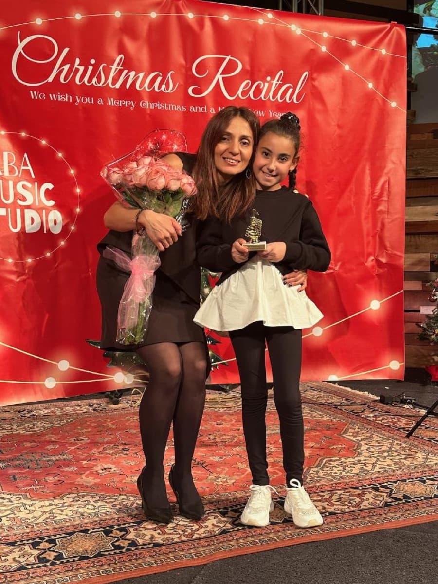A young student holding her recital trophy beside her teacher at the Christmas recital