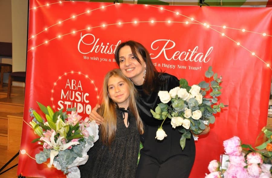 A teacher embracing a young student holding flowers after the recital