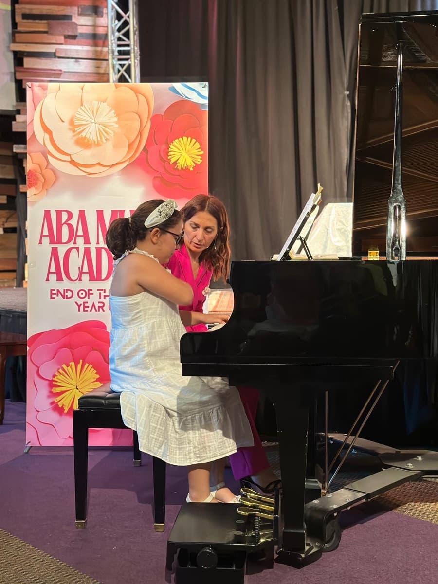 Arpine guiding a young student at the piano on stage
